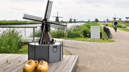Cycling path alongside the windmills of Kinderdijk, with a windmill model and traditional Dutch wooden clogs in the foreground.