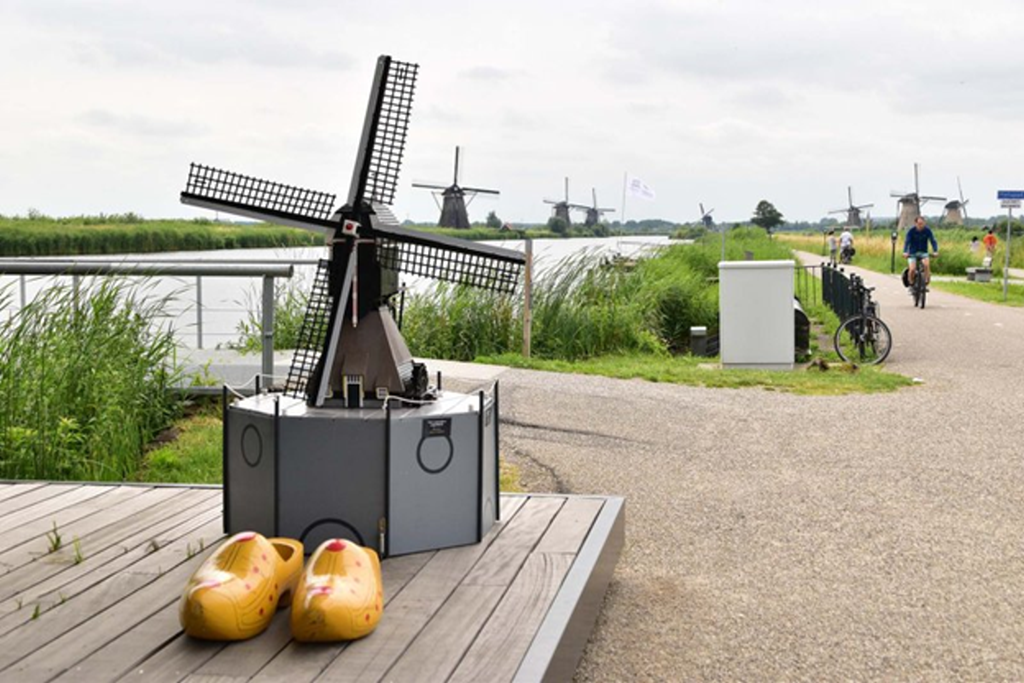 Cycling path alongside the windmills of Kinderdijk, with a windmill model and traditional Dutch wooden clogs in the foreground.